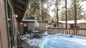 Un jacuzzi en una terraza de madera con vista a una cabaña y árboles.