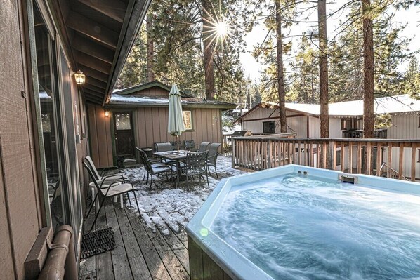 Een hottub op een houten terras met uitzicht op een chalet en bomen.