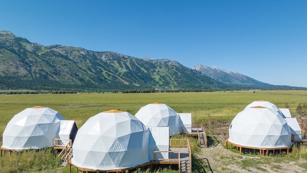 Yurtas en forma de domo geodésico en un campo con montañas al fondo.