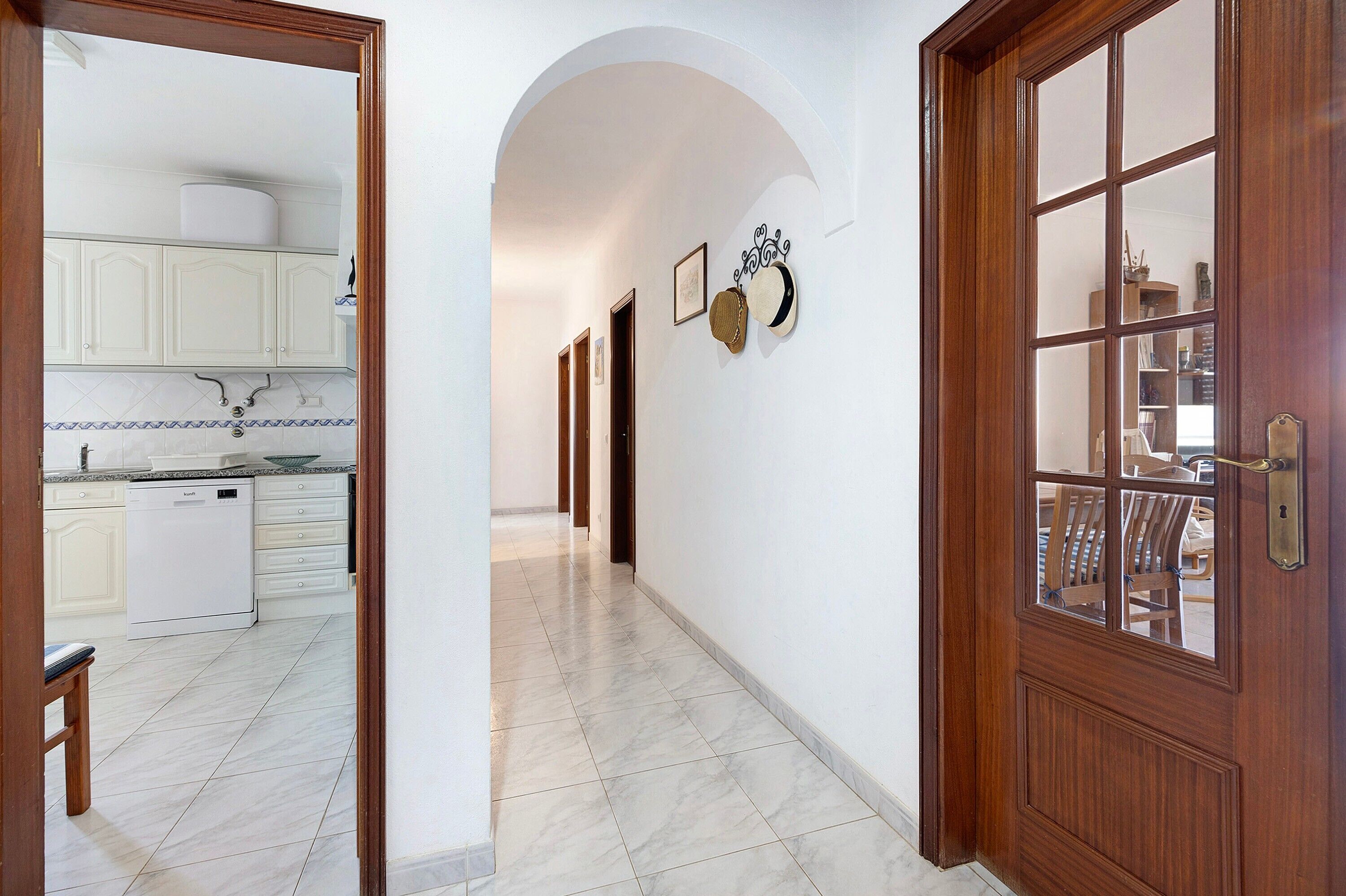A hallway with a kitchen area, wooden doors, and a tiled floor.