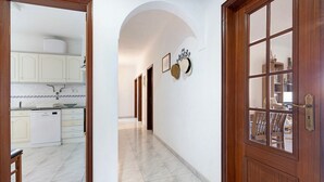 Un pasillo con una zona de cocina, puertas de madera y suelo de baldosas.