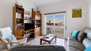 Una sala de estar con un sofá, una silla, una mesa de centro, un televisor y una estantería.