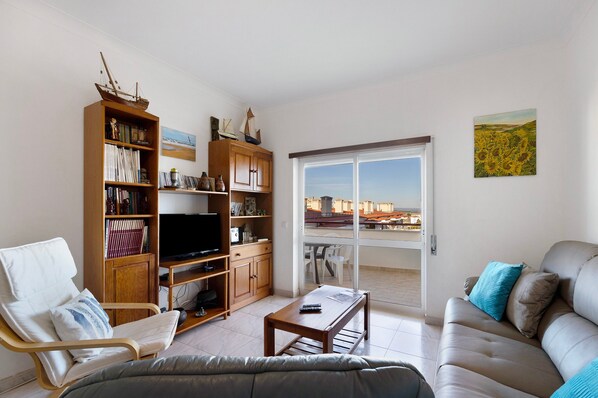 A living room with a sofa, a chair, a coffee table, a TV, and a bookshelf.