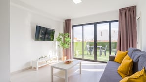 Uma sala de estar moderna com sofá, mesa de centro, televisão e varanda com mesa e cadeiras.
