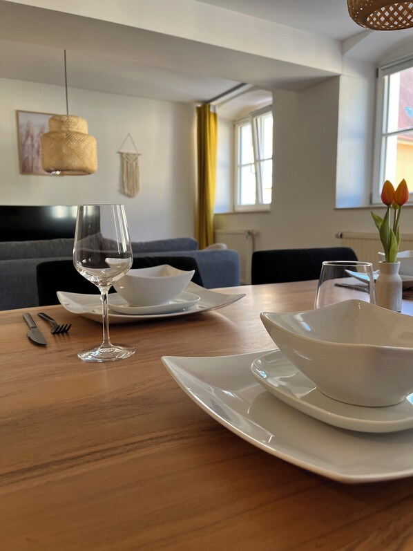 A dining table set with white plates, a wine glass, and cutlery. There is a vase with tulips on the table.