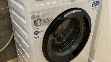 A white front-loading washing machine with a digital display, a control panel, and a hose.