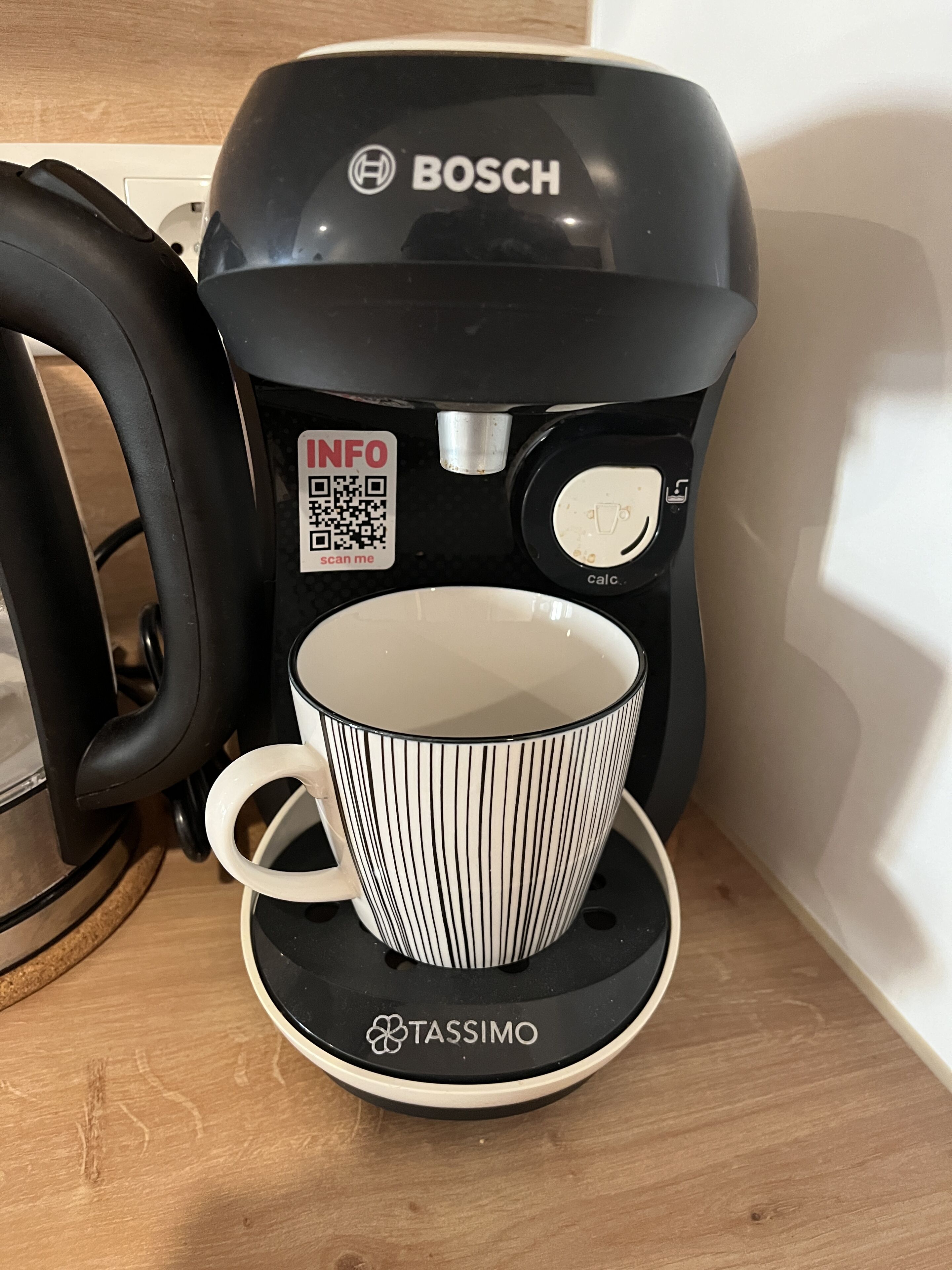 A coffee maker with a cup and saucer on a wooden surface.