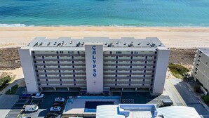 Un parking à étages dont la façade porte l’inscription « CALYPSO », situé juste à côté d’une plage aux eaux d’un bleu limpide.