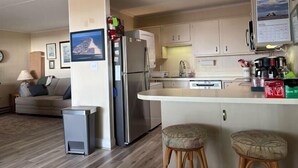 Une cuisine compacte équipée d’un réfrigérateur, d’une cuisinière et d’un évier. On y trouve un petit coin repas avec des tabourets, et un canapé dans le salon.