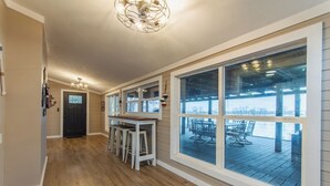 Un pasillo amplio con piso de madera, una zona de bar con taburetes y ventanas grandes que ofrecen vistas a una terraza exterior.
