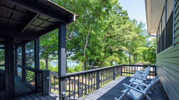 Terraza de madera con mecedoras con vista a un lago, rodeada de árboles.