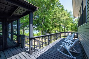 A wooden deck with rocking chairs overlooking a lake, surrounded by trees. - Screened Patio on Pickwick River- Boat & RV Parking, Fishing Pier- Dogs allowed
 (Counce)