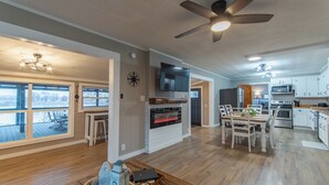 Amplia sala de estar con chimenea, mesa de comedor y cocina con armarios blancos.
