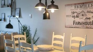A dining area with a table and chairs, pendant lights, and a wall with a 'FARMHOUSE' sign. - Hôtel à la maison - L'Ancrage (Magog)