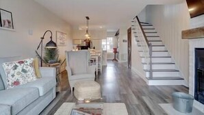 A spacious living room with a sofa, ottoman, and a staircase leading to a dining area. - Hôtel à la maison - L'Ancrage (Magog)
