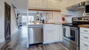 A kitchen with white cabinets, stainless steel appliances, and a wooden floor. - Hôtel à la maison - L'Ancrage (Magog)