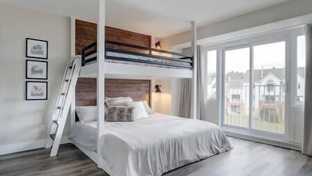 A modern bedroom with a bunk bed, a ladder, a large window, and a view of the outside. - Hôtel à la maison - L'Ancrage (Magog)