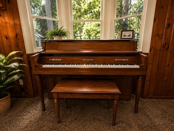 A grand piano with a bench in a room with wooden walls and large windows. - Crest Lodge Historic Mountain Inn (Crestline)