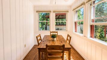 Ein Esszimmer mit Holztisch und -stühlen, großen Fenstern mit Jalousien und einem Deckenventilator.