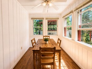 A dining room with a wooden table and chairs, large windows with blinds, and a ceiling fan. - Crest Lodge Historic Mountain Inn (Crestline)