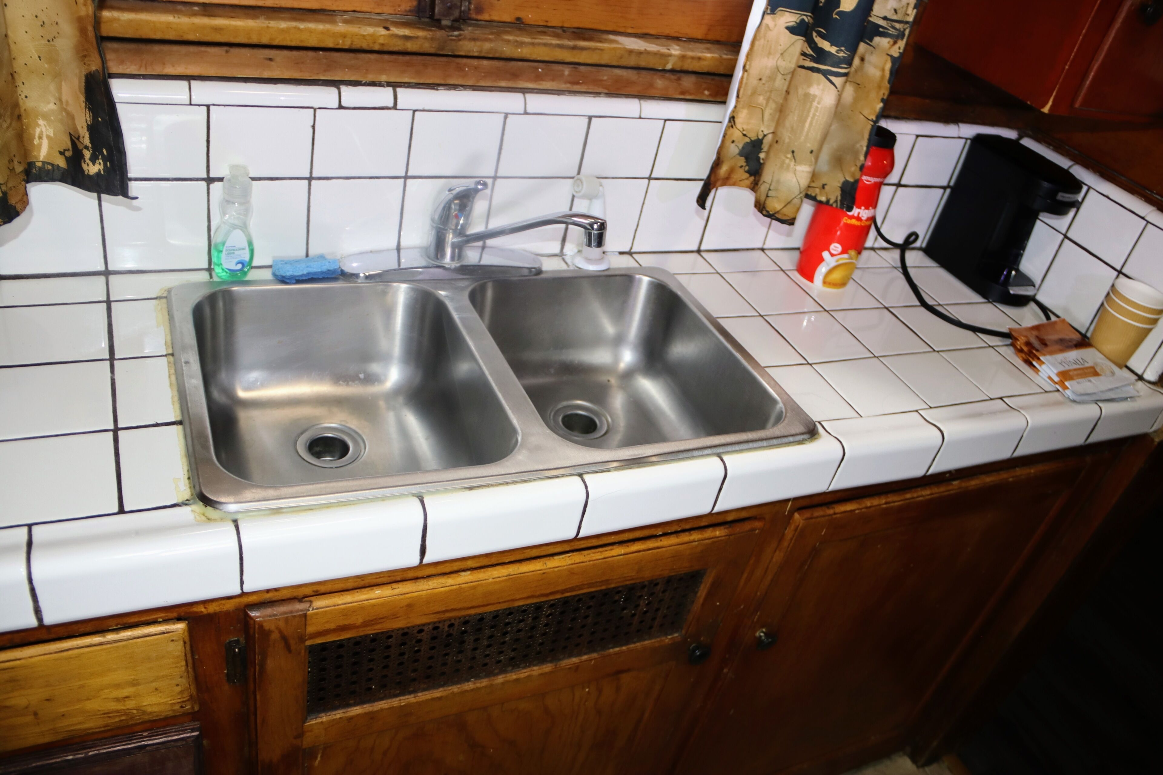 Una cocina con un lavamanos de acero inoxidable doble, una cafetera y una taza de café sobre la encimera.