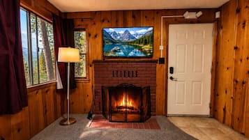 A room with wooden walls, a fireplace, a television mounted above it, and a door to the right.