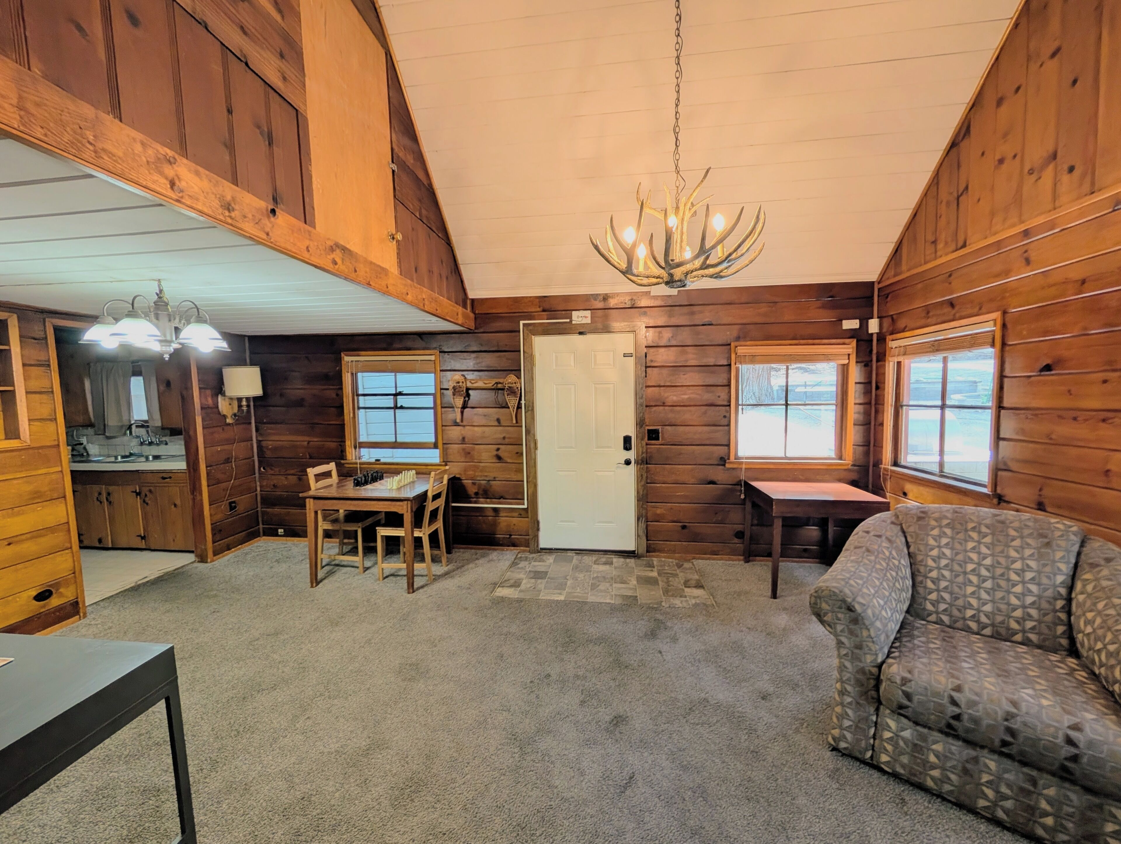 L’intérieur d’une cabane en rondins comprend un coin repas, un canapé, un lustre et une porte.