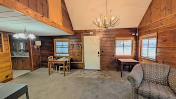 A log cabin interior with a dining area, a sofa, a chandelier, and a door.