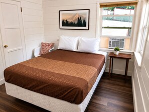 A bedroom with a bed, a window with a view, a bedside table with a plant, and a door. - Crest Lodge Historic Mountain Inn (Crestline)