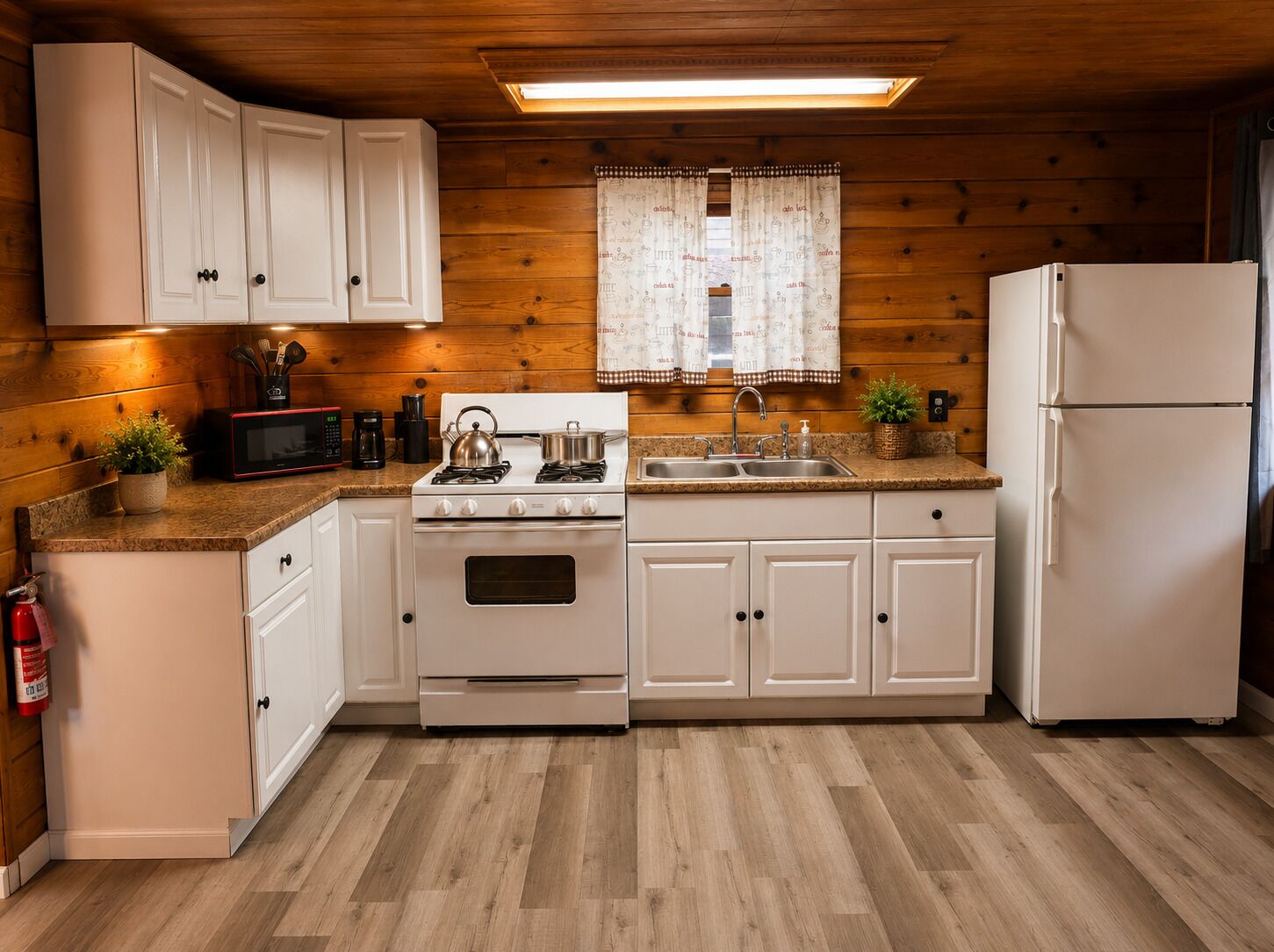 A compact kitchen with white cabinets, a stove, a microwave, a sink, and a refrigerator.