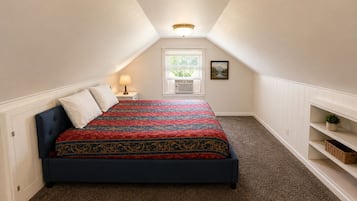 A bedroom with a bed, a nightstand, a lamp, a window with blinds, a picture on the wall, and built-in shelving.