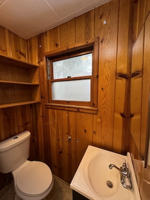 A wooden-paneled bathroom with a toilet, a window, and a sink. - Crest Lodge Historic Mountain Inn (Crestline)