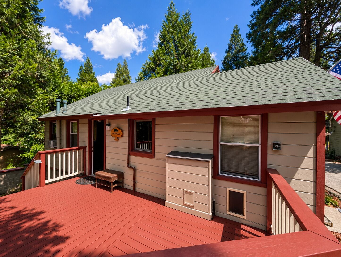 A single-story building with a red deck, a small porch, and a window with a view of the surrounding forest.