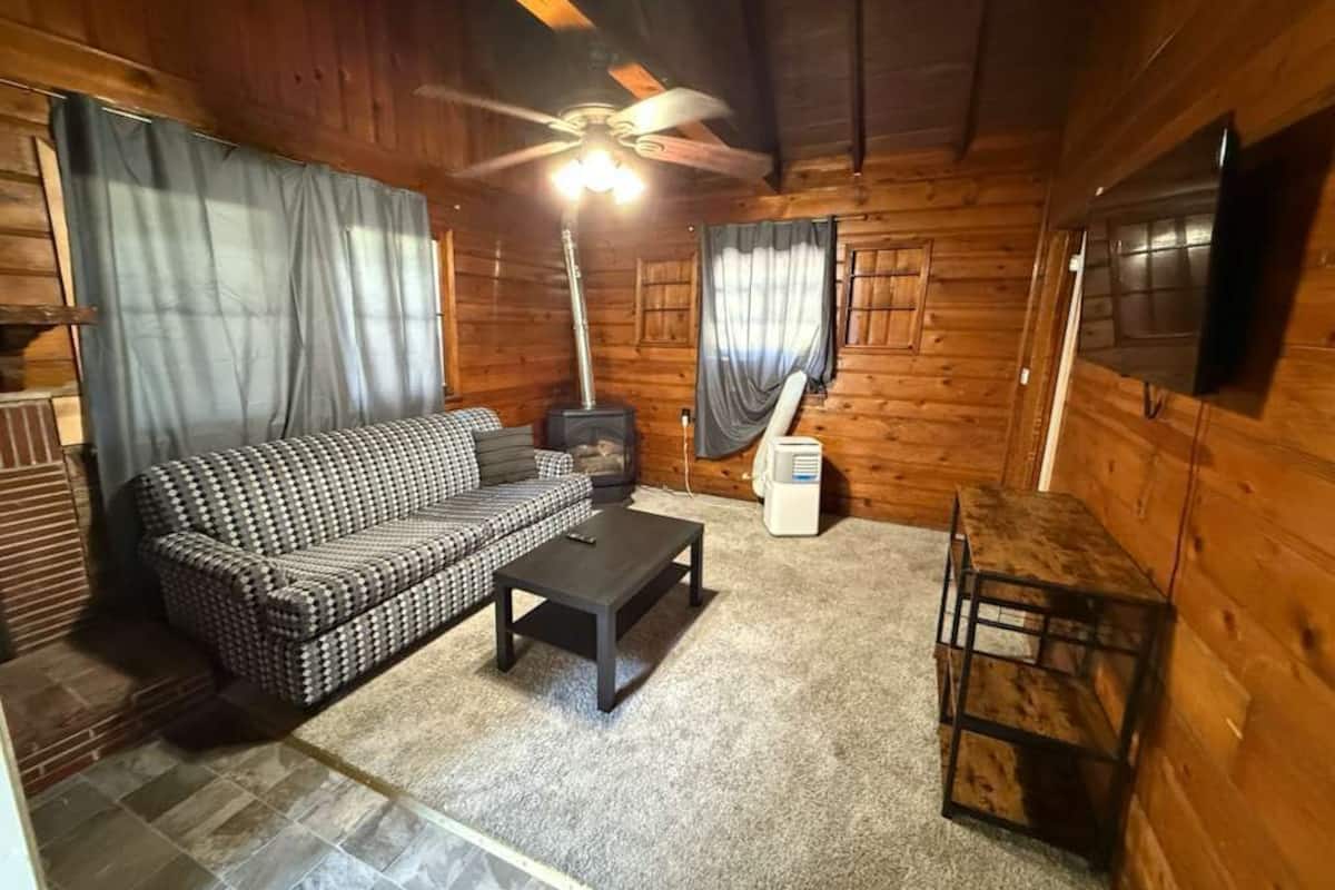 L'intérieur chaleureux d'un chalet avec un canapé à carreaux, une table basse, un ventilateur de plafond et un téléviseur fixé au mur.