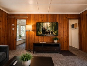 A room with wooden paneling, a large painting of bears, a floor lamp, a dark console table, and a remote control on a coffee table. - Crest Lodge Historic Mountain Inn (Crestline)