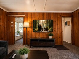 Una habitación con paneles de madera, un cuadro grande de osos, una lámpara de pie, una consola oscura y un control remoto sobre una mesa de centro.