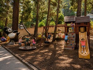 A playground with swings, a slide, and a climbing area. - Crest Lodge Historic Mountain Inn (Crestline)