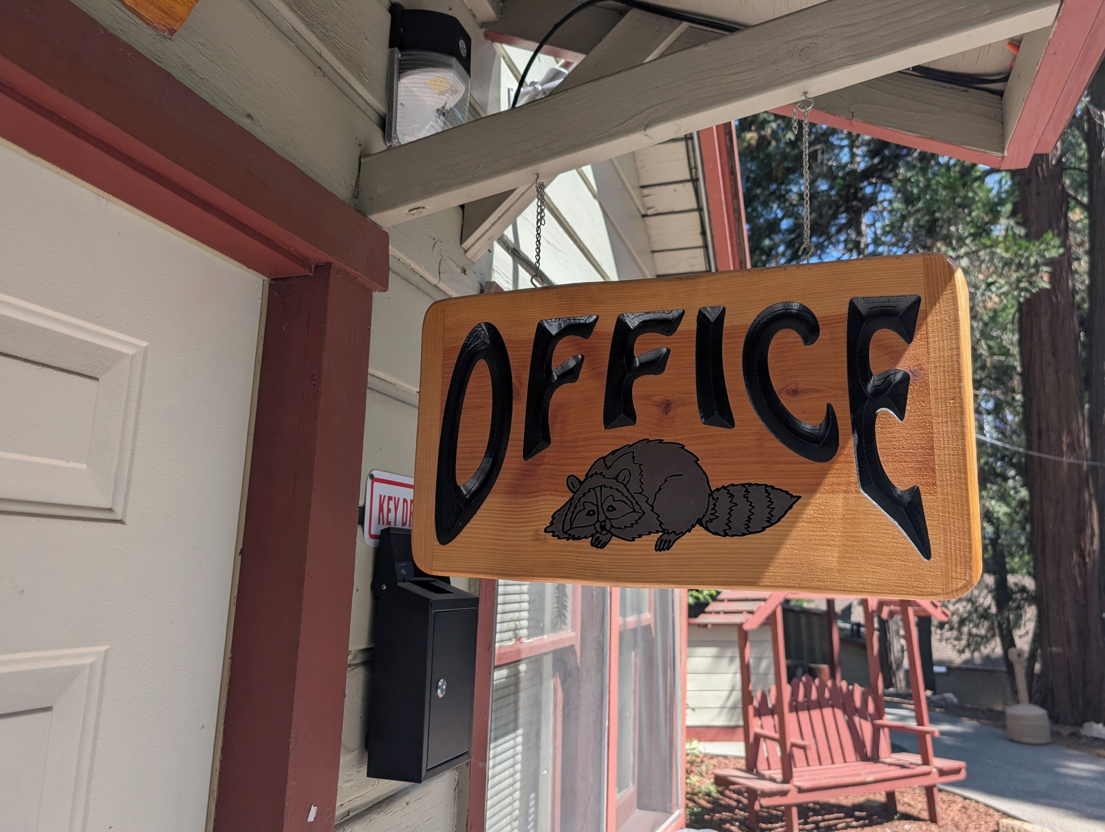 Un letrero de madera con la palabra 'OFFICE' y una ilustración de mapache, sujeto al exterior de un edificio.