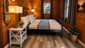 A wooden cabin bedroom with a bed, bedside lamps, a clock, a window, and a welcome sign. - Crest Lodge Historic Mountain Inn (Crestline)
