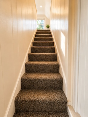 A staircase with carpeted steps leading to a landing with a window and a plant. - Crest Lodge Historic Mountain Inn (Crestline)