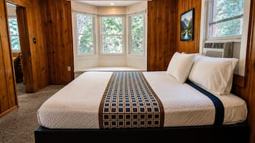 Ein Schlafzimmer mit einem großen Bett, Holzwänden, einem Fenster mit Blick auf Bäume und einer Klimaanlage.