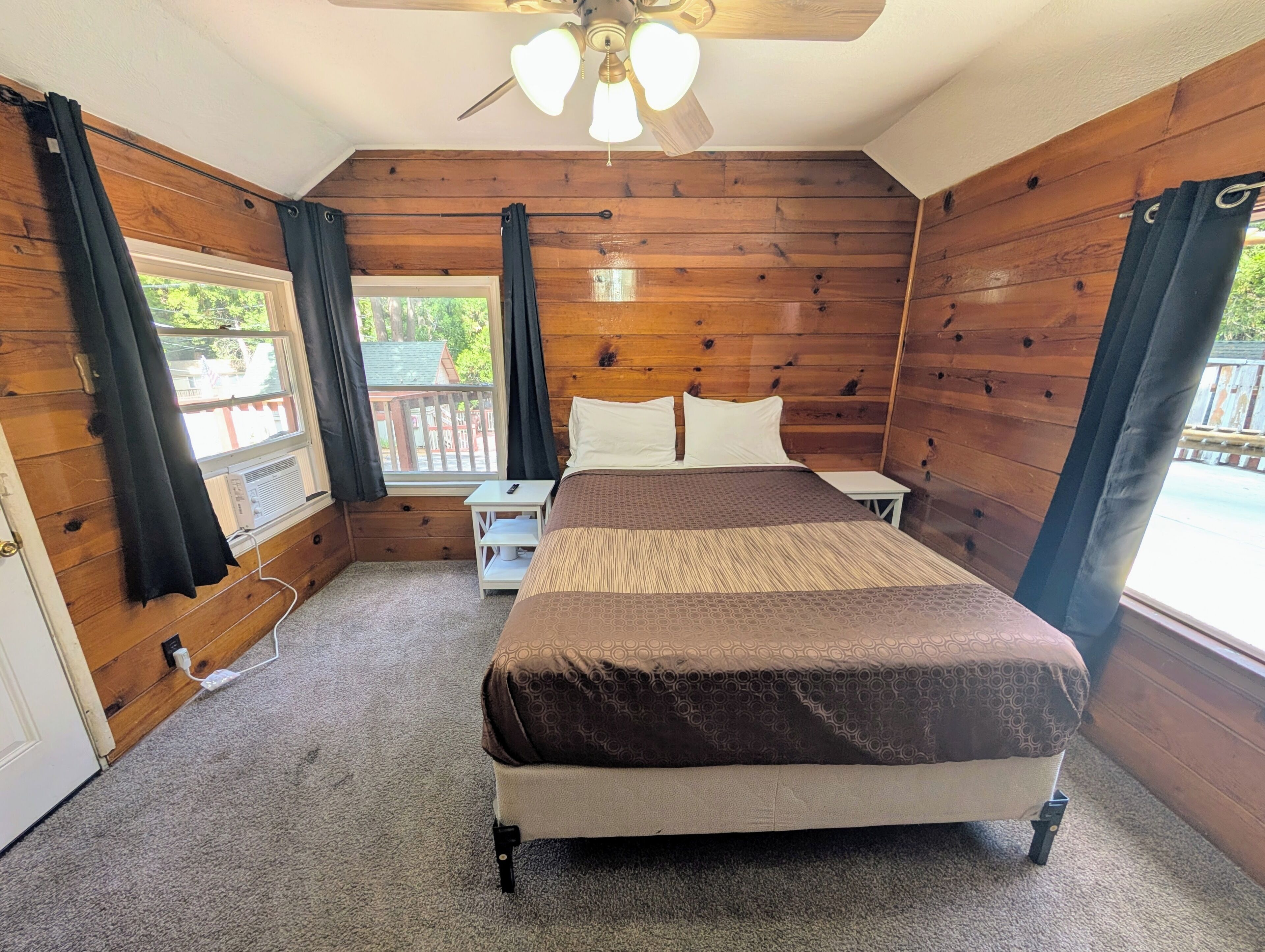 A wooden-paneled bedroom with a bed, bedside tables, a ceiling fan, and a window with curtains.