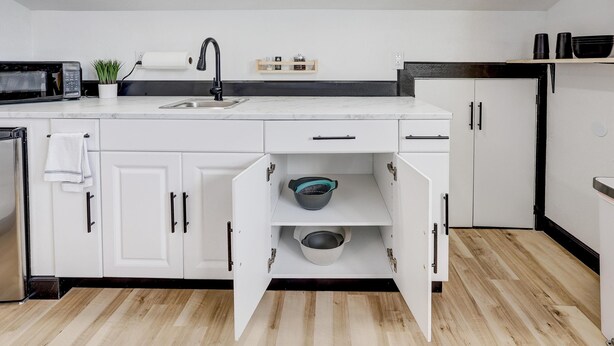 A modern kitchen with white cabinets, a black countertop, and a wooden floor. - The Crow's Nest:  Executive Loft (Webb City)