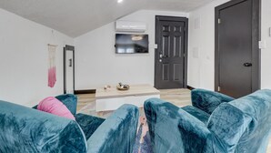 A modern living room with a blue sofa, a small coffee table, and a TV mounted on the wall. - The Crow's Nest:  Executive Loft (Webb City)