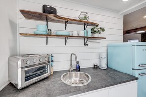 A kitchen with white wooden shelves, a stainless steel sink, a vintage-style stove, and a light blue refrigerator. - The Robin's Egg: Downstairs Studio (Webb City)
