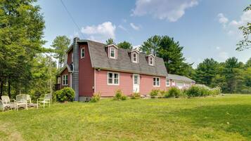 A red house with a sloped roof, a chimney, and a front porch with chairs.