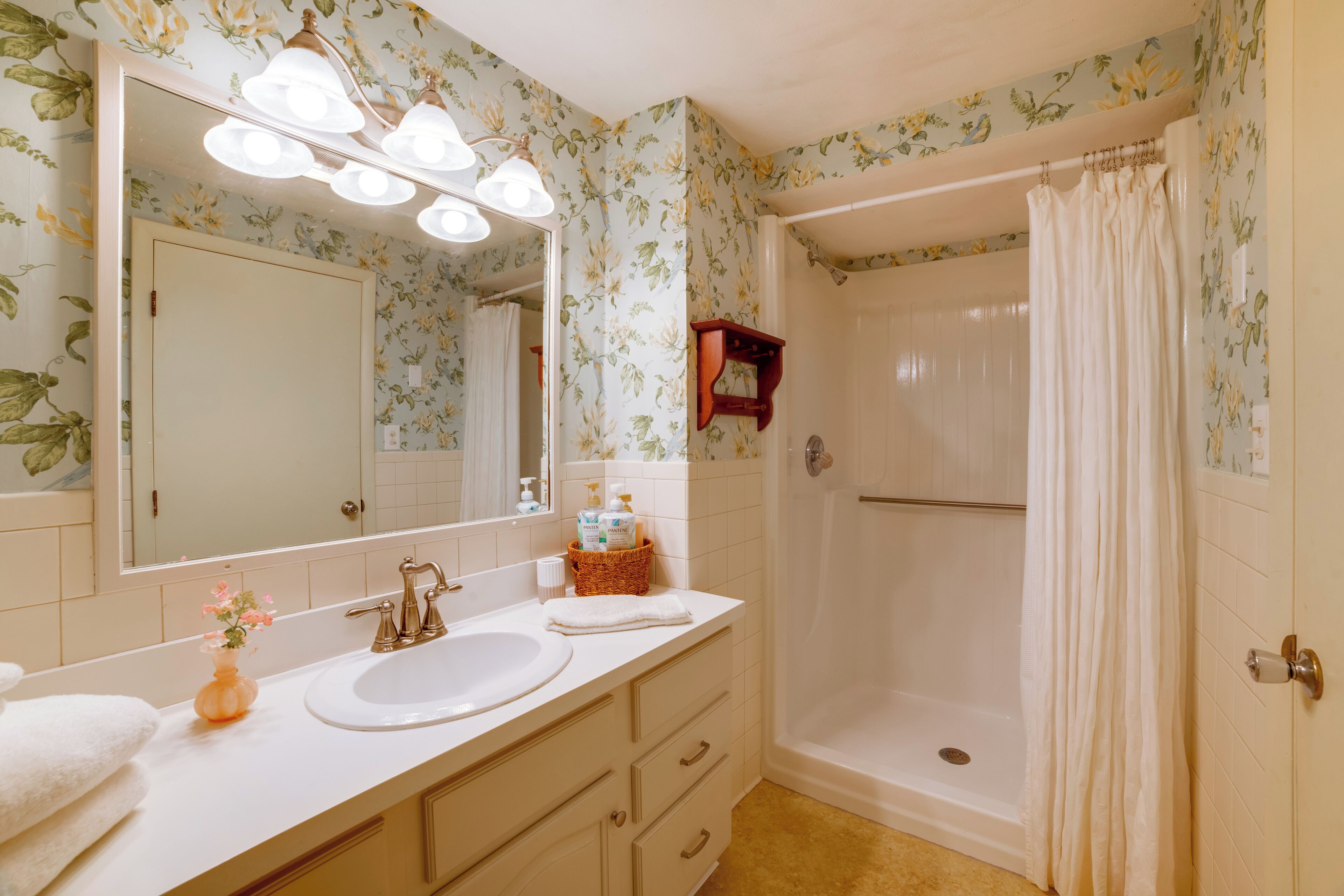 Une salle de bain dotée d’un meuble-lavabo à deux vasques, d’un grand miroir et d’une douche à l’italienne avec rideau.