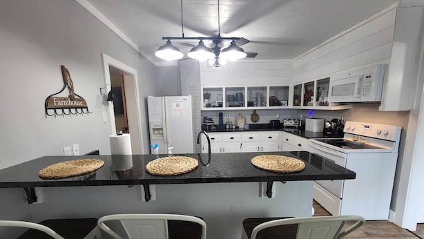 A kitchen with a central island, white cabinets, a microwave, and a stove. There are three chairs at the island and a ceiling fan above. - Pickwick Getaway in the Groves 7th NT Free!
(Counce)