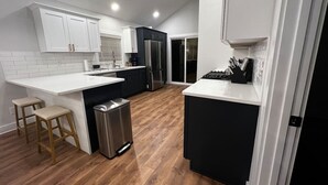 A modern kitchen with white and black cabinetry, a stainless steel refrigerator, and a wooden floor. - Quiet 2 Bedroom home near the Beach! (Sunset Beach)