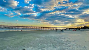A beach with a pier extending into the water, people walking, and a clear sky with clouds. - Quiet 2 Bedroom home near the Beach! (Sunset Beach)